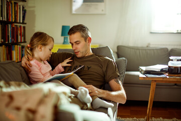 Young father reading with his daughter on the couch after coming back from the army at home