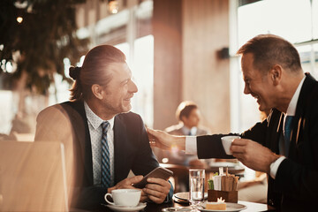 Two Caucasian middle aged businessmen having a meeting over some coffee in a café decorated for Christmas and the new year holidays