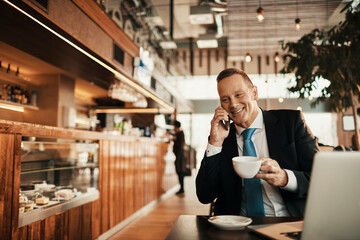 Middle aged businessman talking on a smartphone while having coffee in a cafe decorated for christmas and the new year holidays