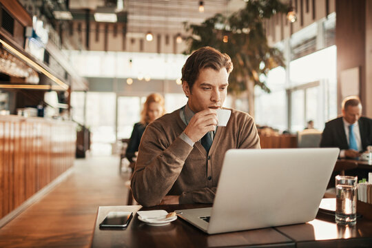 Young businessman enjoying a cup of coffee while working on the laptop in a cafe