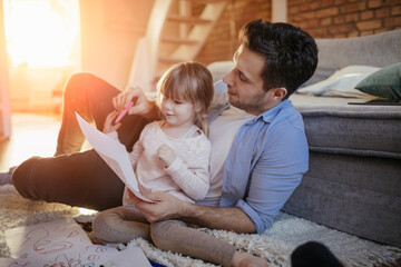 Young father drawing with his daughter on the floor in the living room