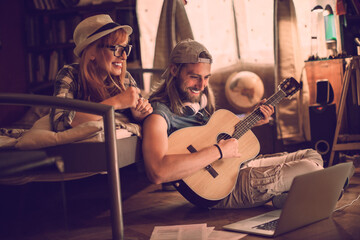 Young man learning how to play the guitar with his girlfriend at home