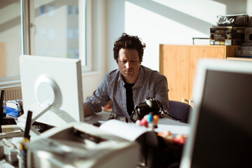 Young Caucasian male photographer going over his work on the computer in a media company office