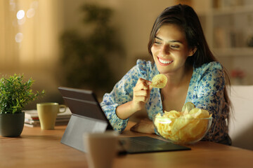 Happy woman in the night watching online content eating chips