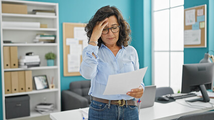 Middle age hispanic woman business worker reading document at the office - obrazy, fototapety, plakaty