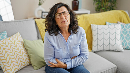 Middle age hispanic woman suffering for stomach ache sitting on sofa at home