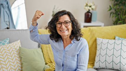 Middle age hispanic woman smiling confident doing strong gesture with arm at home