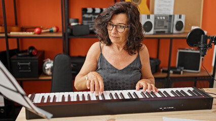 Middle age hispanic woman musician playing piano at music studio