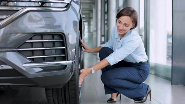 Woman in car showroom choosing a new car and looking on the tires
