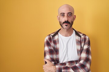 Obraz premium Hispanic man with beard standing over yellow background relaxed with serious expression on face. simple and natural looking at the camera.