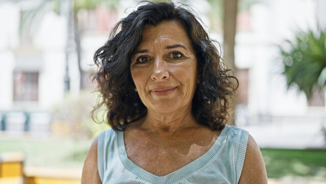 Middle age hispanic woman standing with serious expression at park