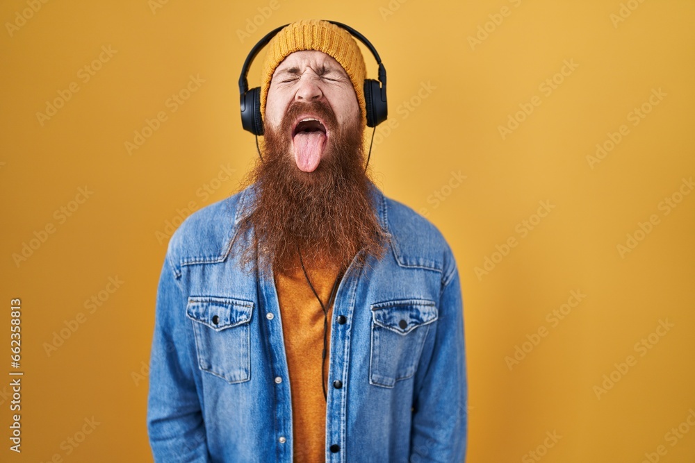 Sticker Caucasian man with long beard listening to music using headphones sticking tongue out happy with funny expression. emotion concept.