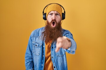 Caucasian man with long beard listening to music using headphones pointing displeased and frustrated to the camera, angry and furious with you
