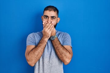 Middle east man with beard standing over blue background shocked covering mouth with hands for mistake. secret concept.