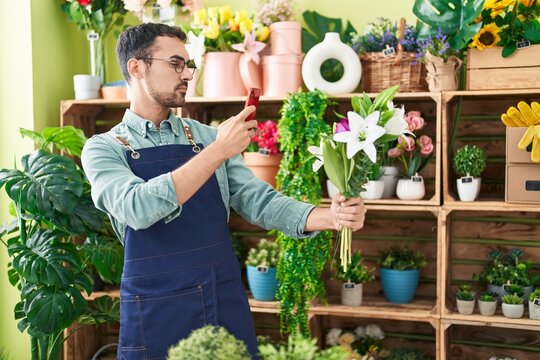 Young hispanic man florist make photo to flowers by smartphone at flower shop