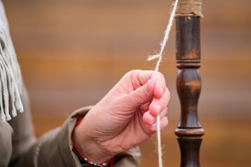 Close up of woman's hands weaving a thread on a spinning wheel. The woman carefully spins the wool...