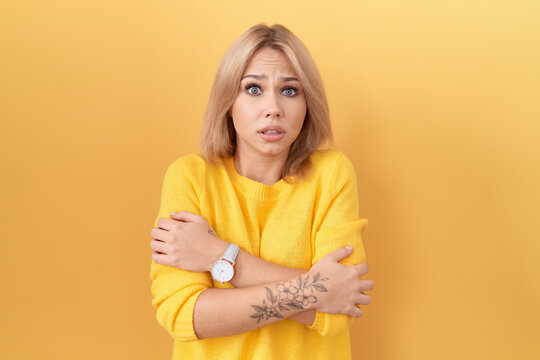 Young caucasian woman wearing yellow sweater shaking and freezing for winter cold with sad and shock expression on face