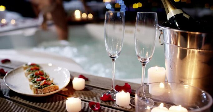 Champagne glass, food and hot tub couple arrive, enter and romantic partner bonding on Valentines day date. France holiday night, candle flame and marriage people enter jacuzzi with alcohol and snack