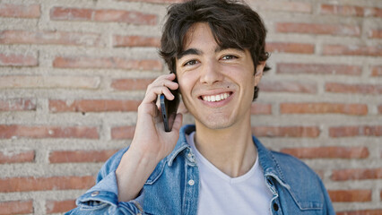 Young hispanic man smiling confident talking on the smartphone over isolated brick background