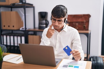 Young hispanic man working using computer laptop holding credit card pointing to the eye watching you gesture, suspicious expression