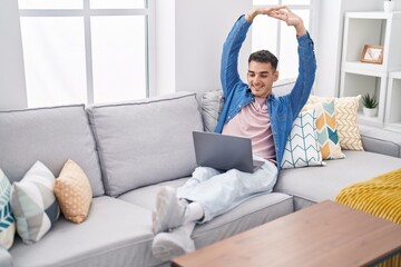 Young hispanic man stretching arms using laptop at home