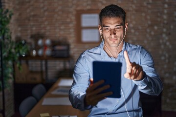 Handsome hispanic man working at the office at night pointing with finger up and angry expression, showing no gesture - obrazy, fototapety, plakaty