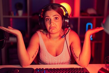 Young blonde woman playing video games wearing headphones clueless and confused expression with arms and hands raised. doubt concept. © Krakenimages.com