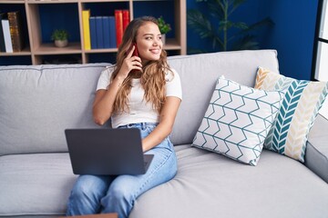 Fototapeta premium Young beautiful hispanic woman talking on smartphone using laptop at home