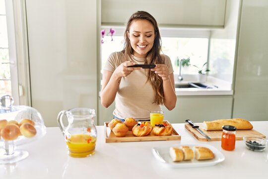 Young beautiful hispanic woman make photo by smartphone to breakfast at the kitchen