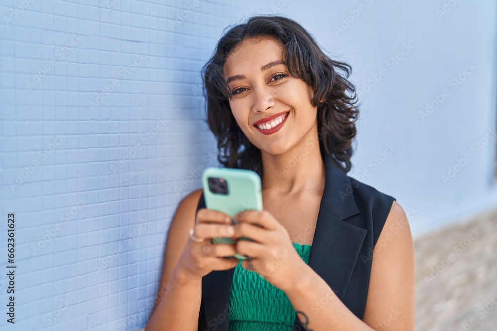 Sticker Young beautiful hispanic woman smiling confident using smartphone at street