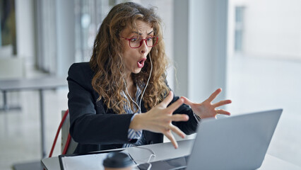 Young woman business worker using laptop and earphones stressed at the office