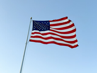 US American flag waving in the wind with a blue sky in background