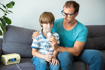 Dad helps his sick child do inhalation with a nebulizer at home: he holds a mask from which steam....