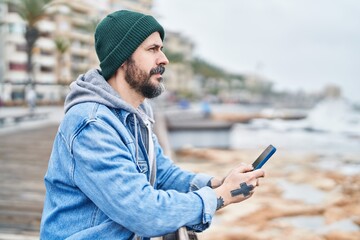 Young bald man using smartphone with serious expression at seaside