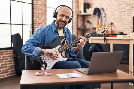 Young bald man musician having online electrical guitar lesson at music studio
