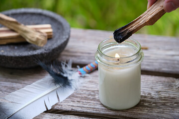 A woman's hand is lighting a palo santo stick on a candle flame outdoors in the garden in summer