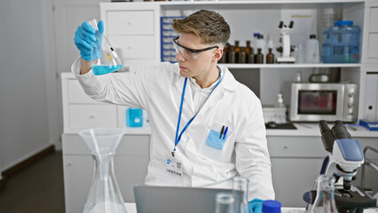 Young caucasian man scientist measuring liquid on test tube using laptop at laboratory