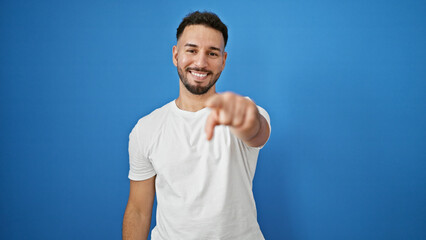Young arab man smiling confident pointing with finger to the camera over isolated blue background
