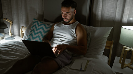 Young arab man using laptop sitting on the bed at bedroom