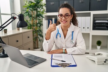 Young hispanic woman wearing doctor uniform and stethoscope doing happy thumbs up gesture with hand. approving expression looking at the camera showing success.