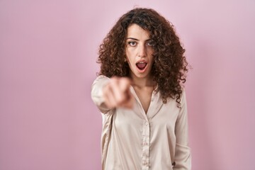 Fototapeta premium Hispanic woman with curly hair standing over pink background pointing displeased and frustrated to the camera, angry and furious with you