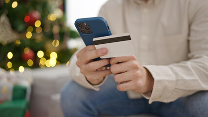 Young hispanic man shopping with smartphone and credit card celebrating christmas at home