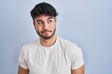 Hispanic man with beard standing over white background smiling looking to the side and staring away thinking.