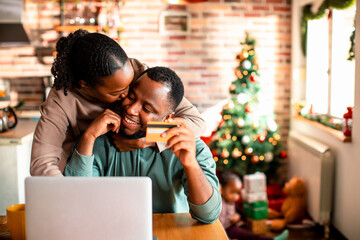Young African American couple online shopping for presents on a laptop at their home decorated for the Christmas and new year holidays