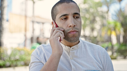 Young hispanic man speaking on the phone looking serious at park