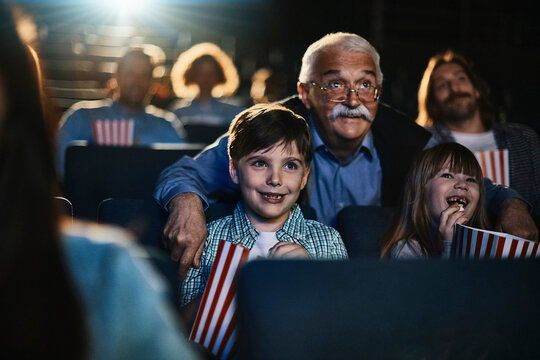 Young children watching a movie with their grandfather in the cinema
