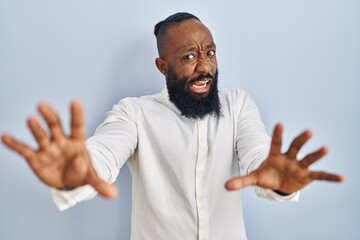 African american man standing over blue background afraid and terrified with fear expression stop gesture with hands, shouting in shock. panic concept.