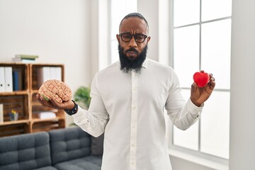 African american man working at therapy office holding brain and heart puffing cheeks with funny face. mouth inflated with air, catching air. - obrazy, fototapety, plakaty