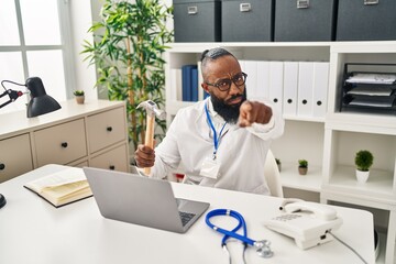 African american man working at medical clinic holding hammer pointing with finger to the camera and to you, confident gesture looking serious