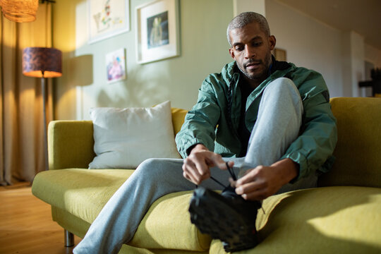 Middle aged African American man tying his shoelaces and getting ready at home to go jogging and exercising outside